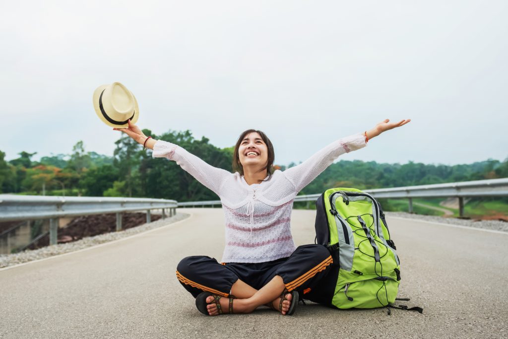 young asian woman traveler with backpack relaxing sitting road